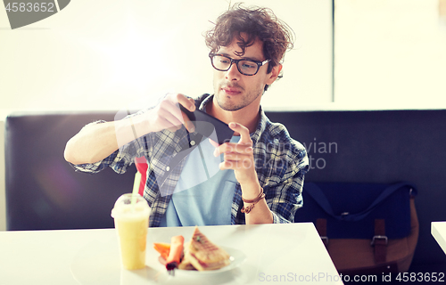 Image of man with smartphone photographing food at cafe