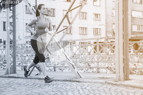 Image of woman jogging across the bridge at sunny morning