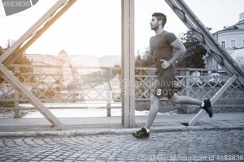 Image of man jogging across the bridge at sunny morning