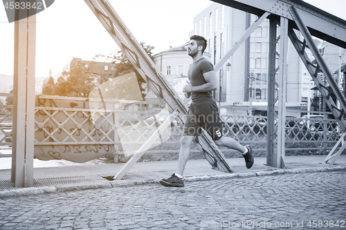 Image of man jogging across the bridge at sunny morning