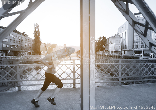 Image of woman jogging across the bridge at sunny morning