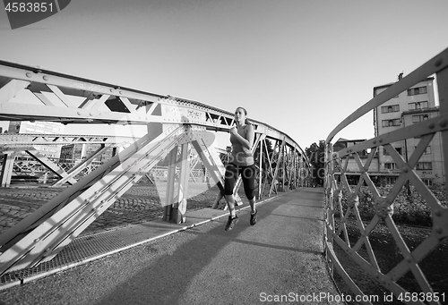 Image of woman jogging across the bridge at sunny morning