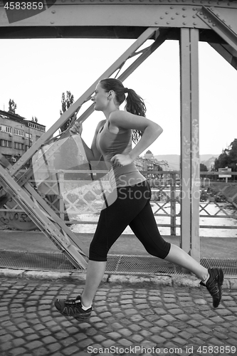 Image of woman jogging across the bridge at sunny morning