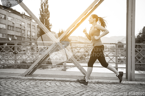 Image of woman jogging across the bridge at sunny morning