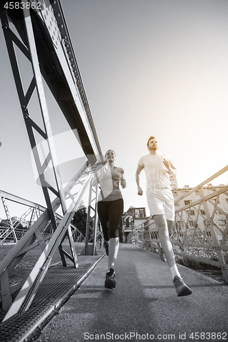 Image of young couple jogging across the bridge in the city