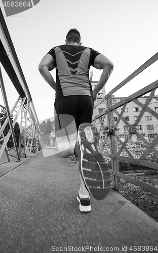 Image of man jogging across the bridge at sunny morning