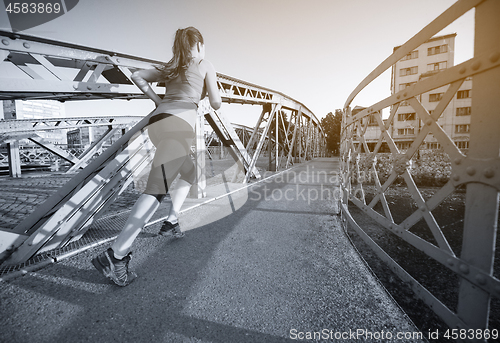 Image of woman jogging across the bridge at sunny morning