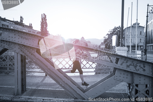 Image of woman jogging across the bridge at sunny morning