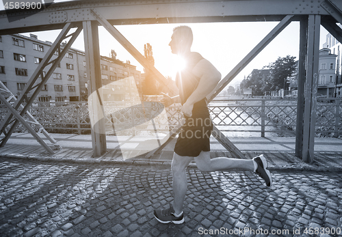 Image of man jogging across the bridge at sunny morning