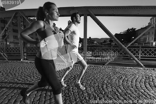 Image of couple jogging across the bridge in the city