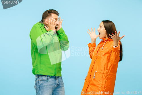 Image of The young surprised couplel posing at studio in autumn jackets isolated on blue