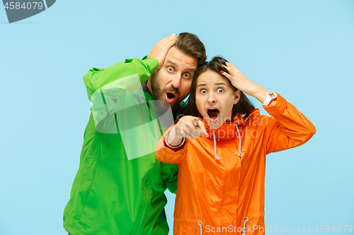 Image of The young surprised couplel posing at studio in autumn jackets isolated on blue