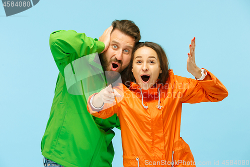 Image of The young surprised couplel posing at studio in autumn jackets isolated on blue