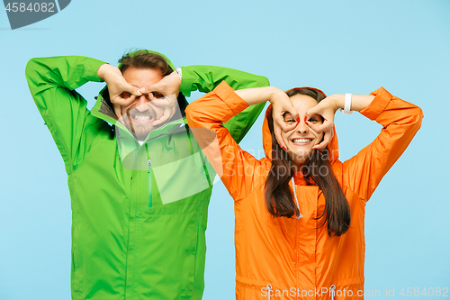 Image of The young surprised couplel posing at studio in autumn jackets isolated on blue