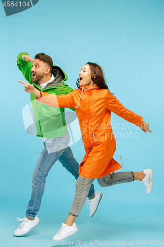 Image of The young surprised couplel posing at studio in autumn jackets isolated on blue