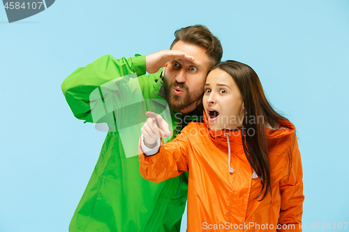 Image of The young surprised couplel posing at studio in autumn jackets isolated on blue