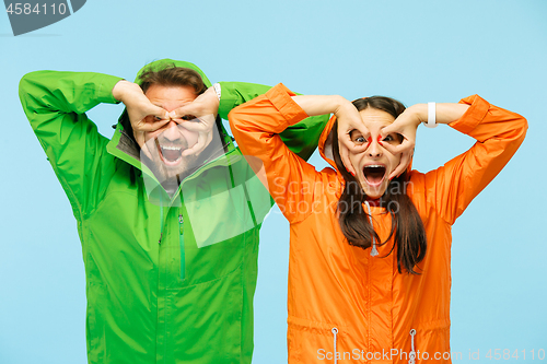 Image of The young surprised couplel posing at studio in autumn jackets isolated on blue