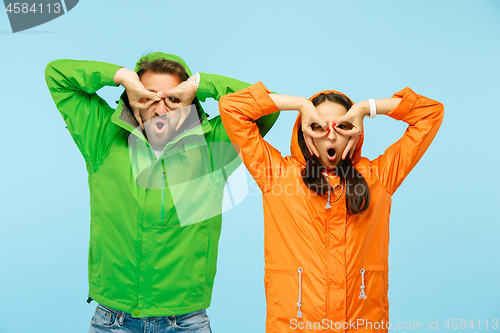 Image of The young surprised couplel posing at studio in autumn jackets isolated on blue