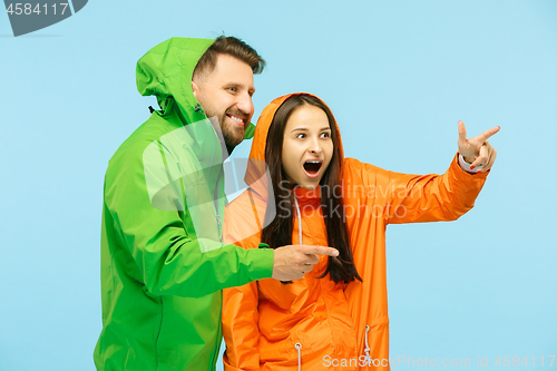 Image of The young surprised couplel posing at studio in autumn jackets isolated on blue