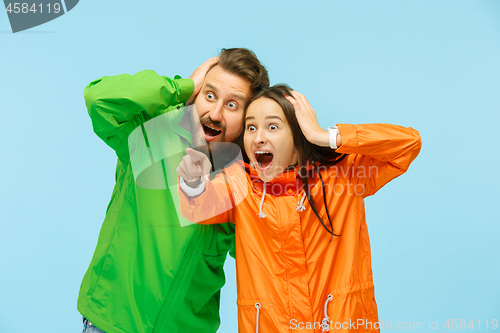 Image of The young surprised couplel posing at studio in autumn jackets isolated on blue