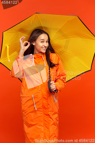 Image of The young girl posing at studio in autumn jacket isolated on red