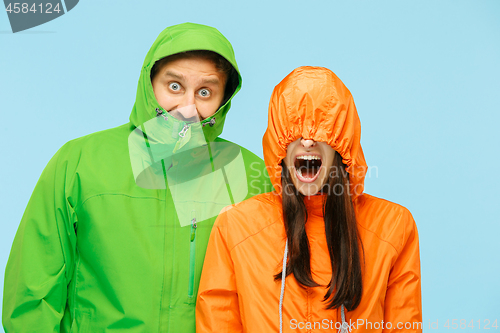 Image of The young surprised couplel posing at studio in autumn jackets isolated on blue