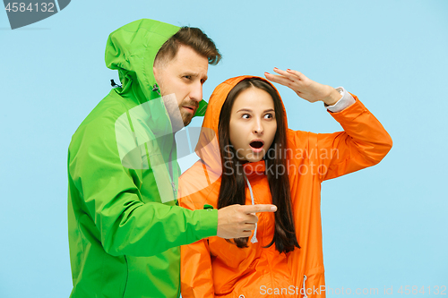 Image of The young surprised couplel posing at studio in autumn jackets isolated on blue