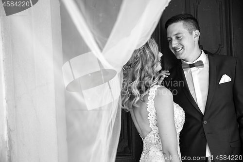 Image of Groom hugs bride tenderly in the shadow of a flying veil.