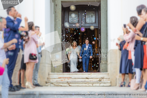 Image of Newlyweds exiting the church after the wedding ceremony, family and friends celebrating their love with the shower of soap bubbles, custom undermining traditional rice bath