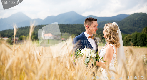 Image of Groom hugs bride tenderly in wheat field somewhere in Slovenian countryside.