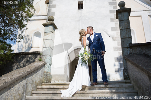 Image of The Kiss. Bride and groom kisses tenderly on a staircase in front of a small local church.