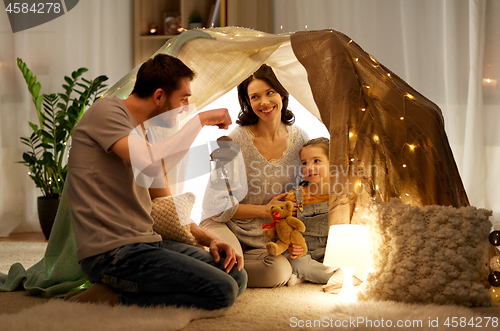 Image of happy family playing in kids tent at night at home