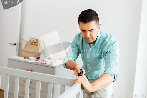 Image of happy father with screwdriver assembling baby bed