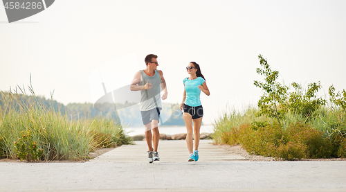 Image of couple in sports clothes running along beach path