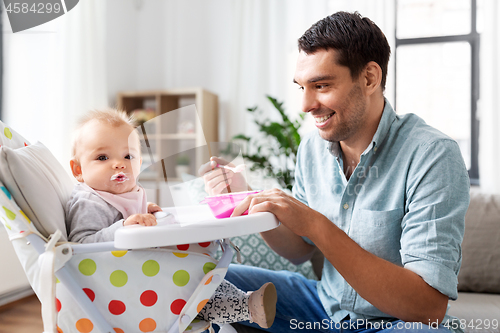 Image of father feeding happy baby in highchair at home