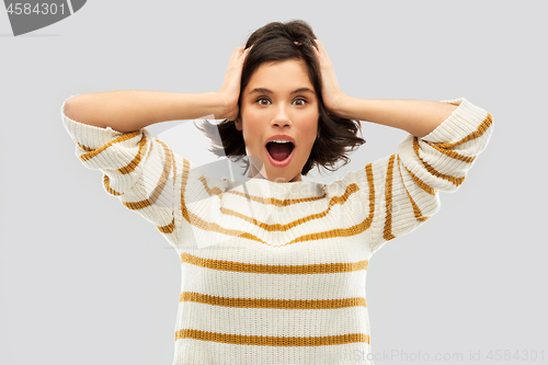 Image of impressed woman in pullover holding to her head