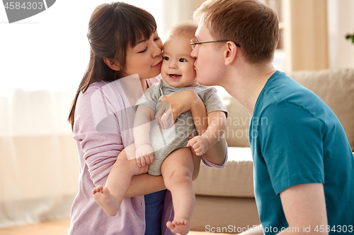 Image of happy mother and father kissing baby son at home