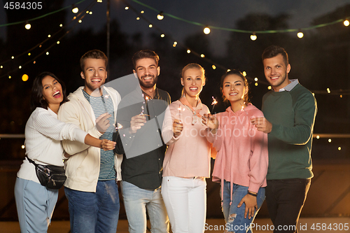 Image of happy friends with sparklers at rooftop party