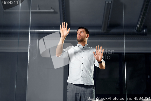 Image of businessman touching glass wall at night office