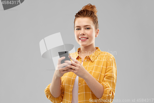 Image of smiling red haired teenage girl using smartphone