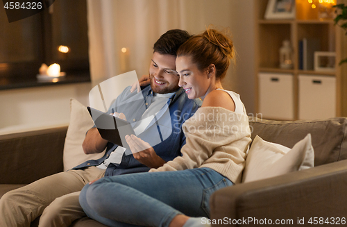 Image of happy couple using tablet pc at home in evening