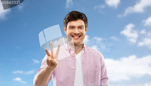 Image of young man showing three fingers over sky