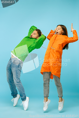 Image of The young surprised couplel posing at studio in autumn jackets isolated on blue