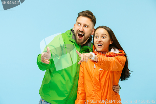 Image of The young surprised couplel posing at studio in autumn jackets isolated on blue