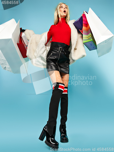 Image of Full length portrait of a beautiful smiling woman walking with colorful shopping bags isolated over blue background
