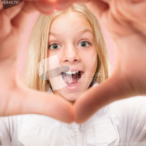 Image of Beautiful smiling teen girl makes the shape of a heart with her hands on the pink background.