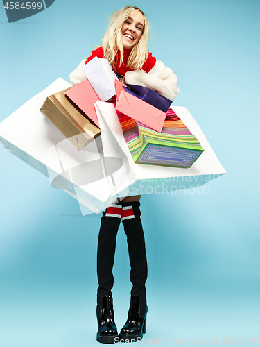 Image of Full length portrait of a beautiful smiling woman walking with colorful shopping bags isolated over blue background