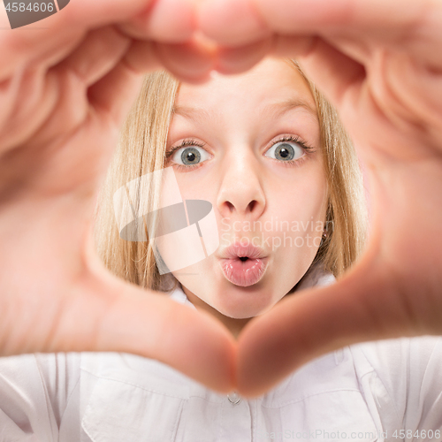 Image of Beautiful smiling teen girl makes the shape of a heart with her hands on the pink background.