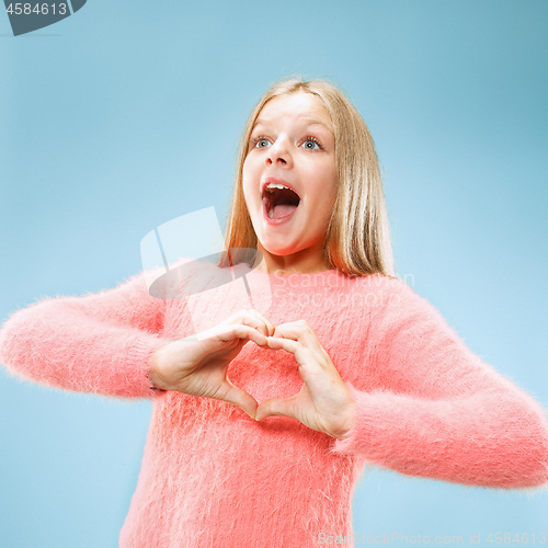 Image of Beautiful smiling teen girl makes the shape of a heart with her hands on the blue background.