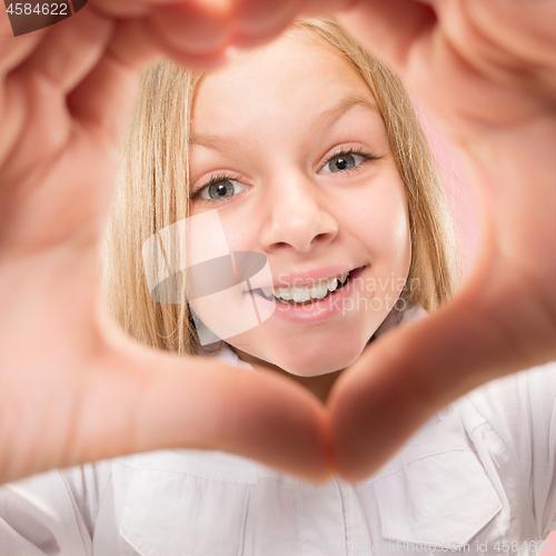 Image of Beautiful smiling teen girl makes the shape of a heart with her hands on the pink background.